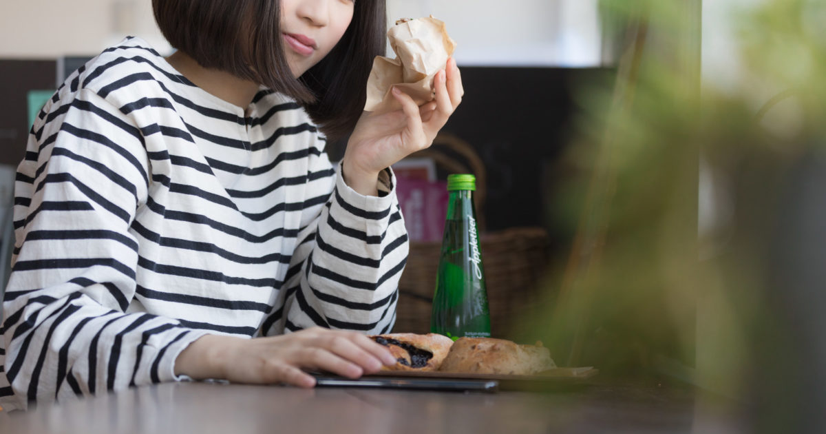 パンを食べながらスマホで売上をチェックする女性