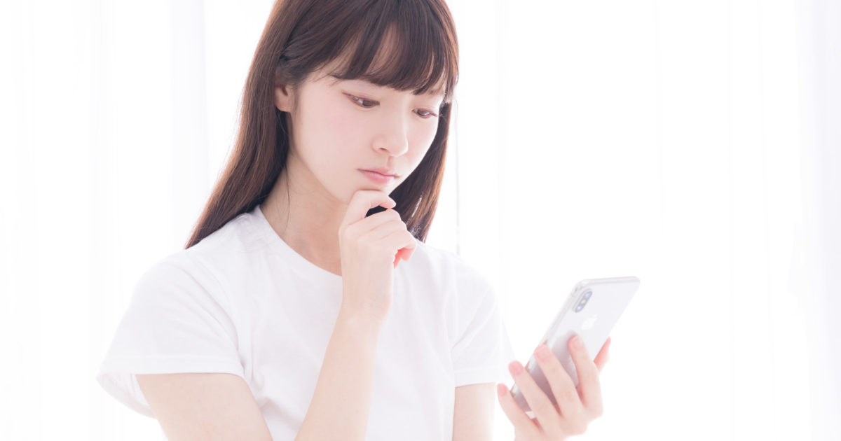 なぜ売れないのかスマホを眺めて考え込む白いTシャツの女性