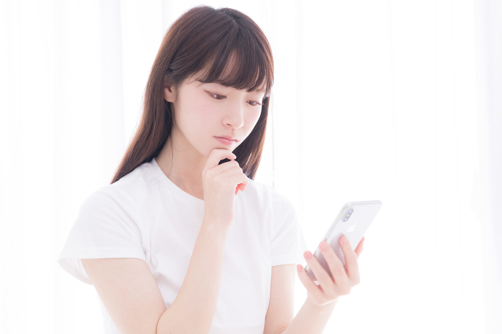 なぜ売れないのかスマホを眺めて考え込む白いTシャツの女性