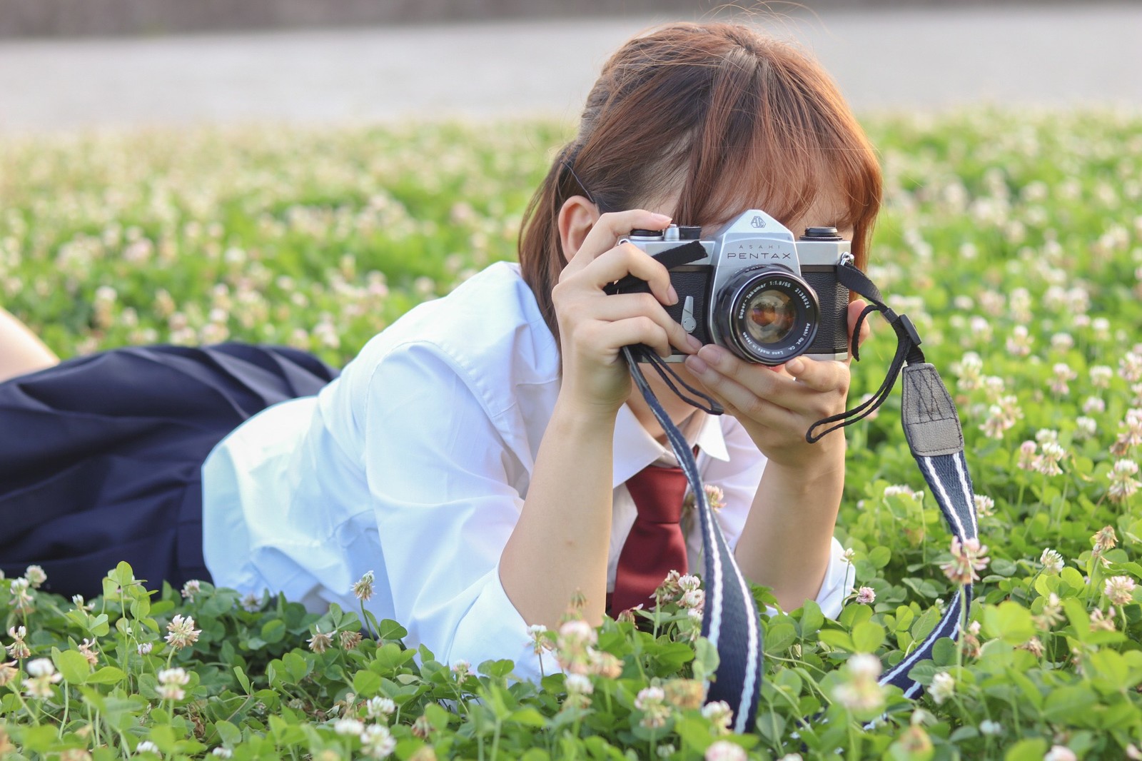 草原にうつ伏せてカメラを構える女子高生