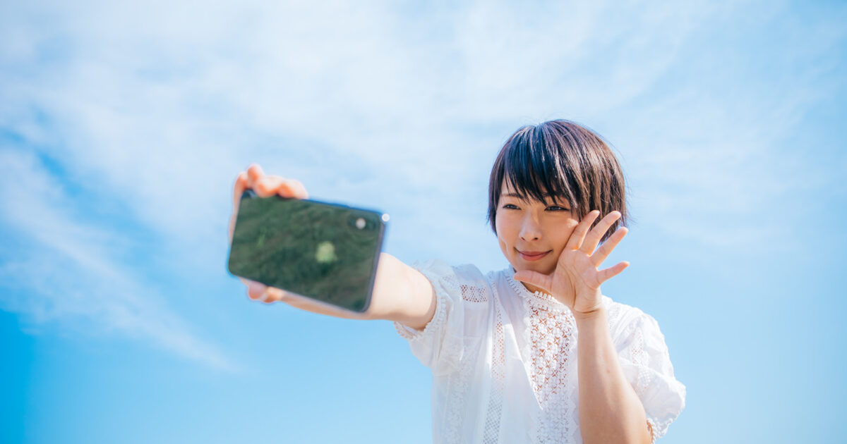青空の下でスマホで自撮りする女子