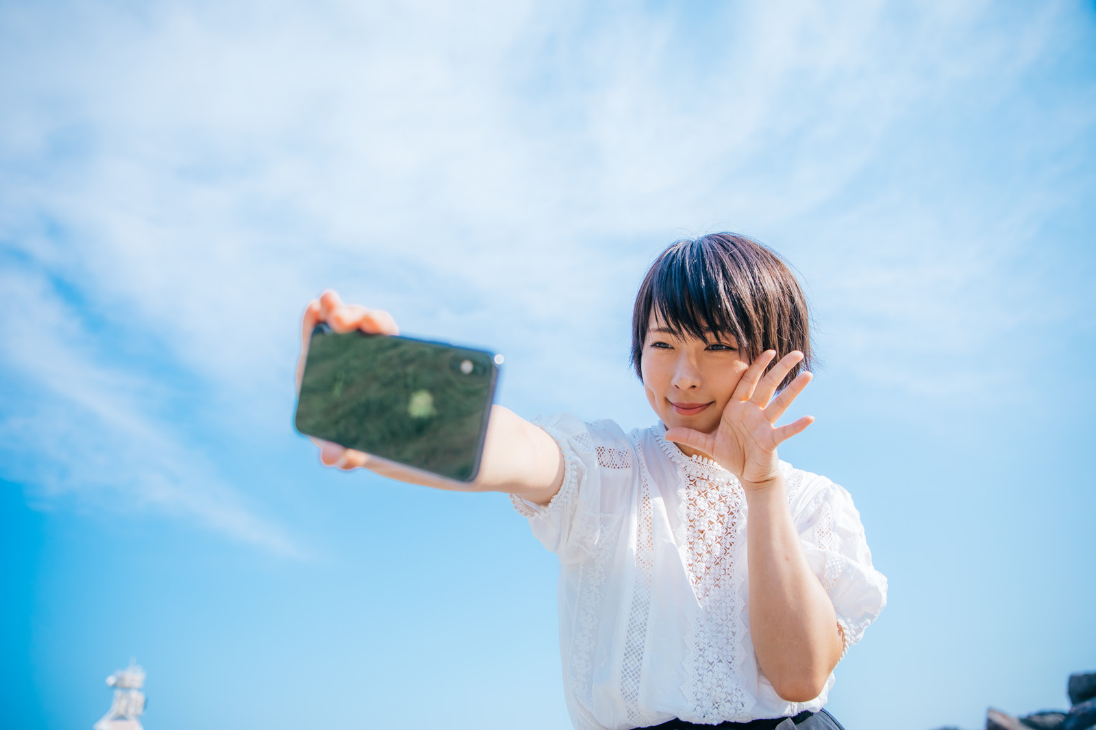 青空の下でスマホで自撮りする女子